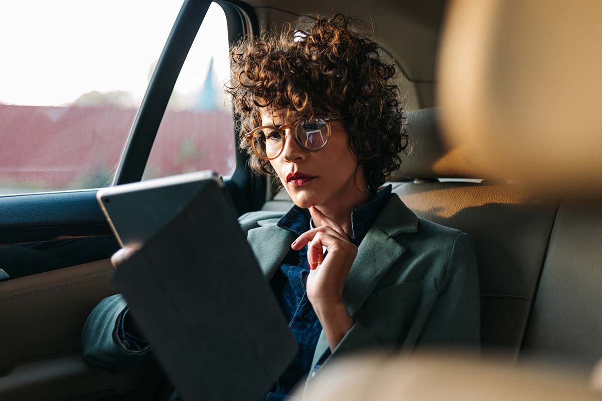 A women with glasses, sitting in a moving car, looking interesting in her Tablet